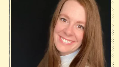 A headshot of a smiling woman with red hair.