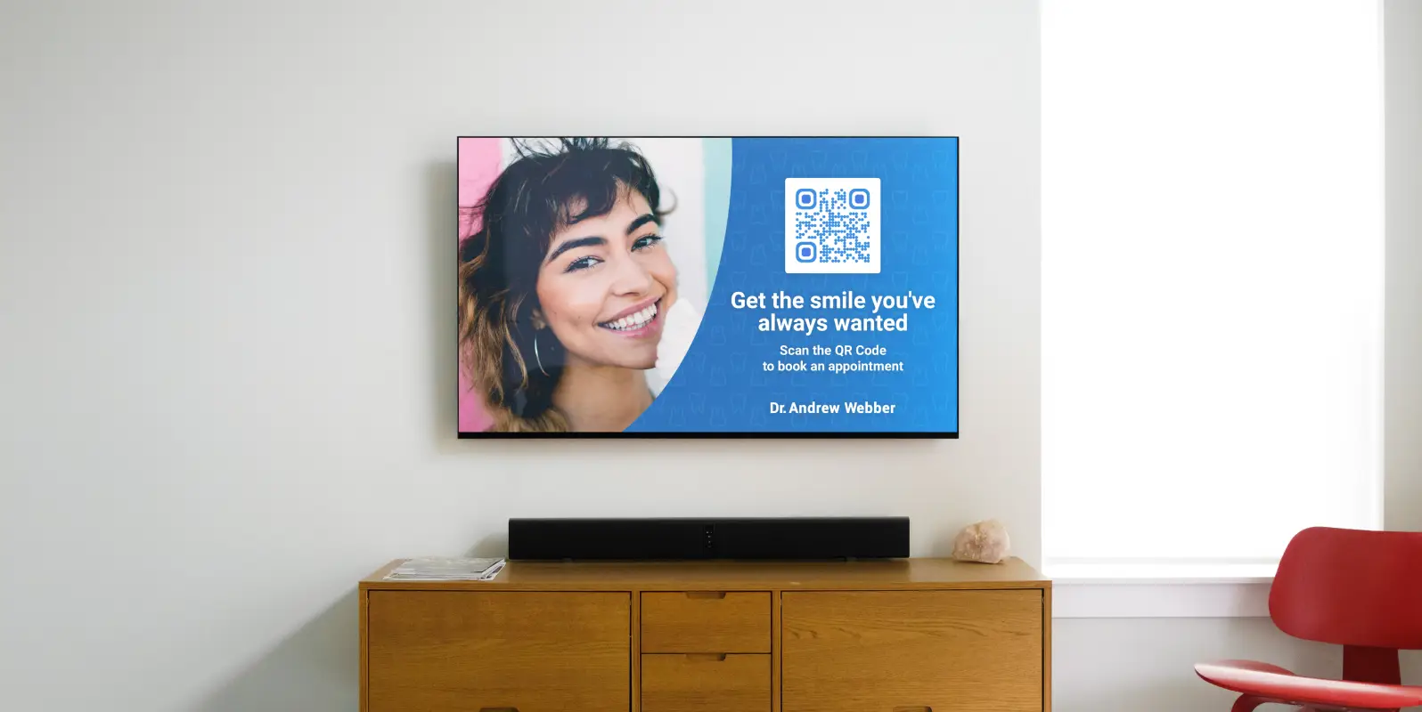 A TV on a wall with a dentists's ad showing a woman smiling and a QR Code that can be scanned to book an appointment. There's a table below the TV with a sound bar on it.